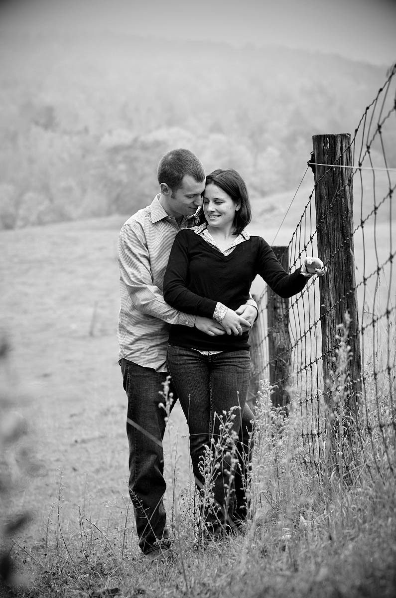 Young couple in farm field by fence at country themed engagement session