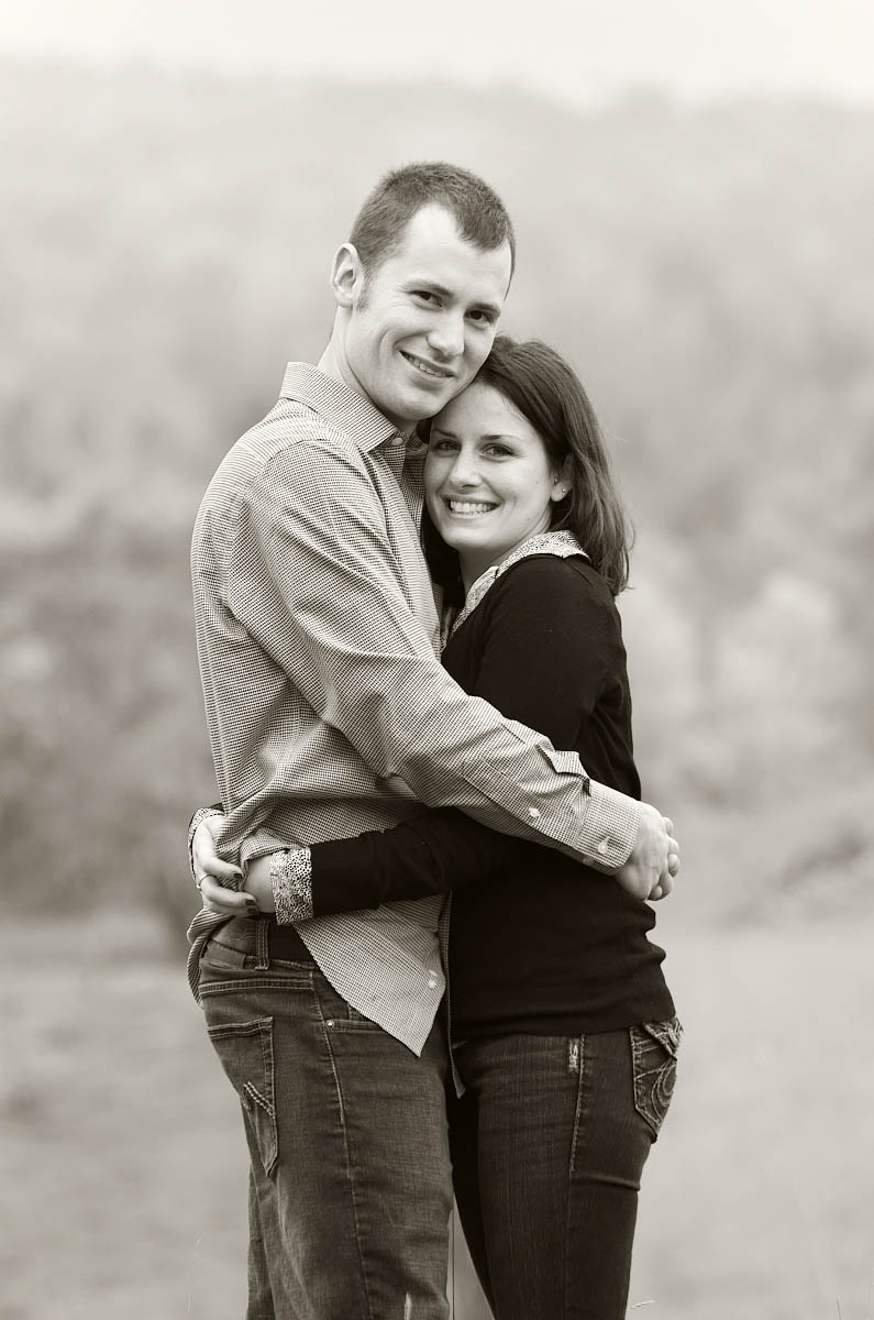 Young couple hugs in farm field at country themed engagement session in Omemee, Ontario near Lindsay