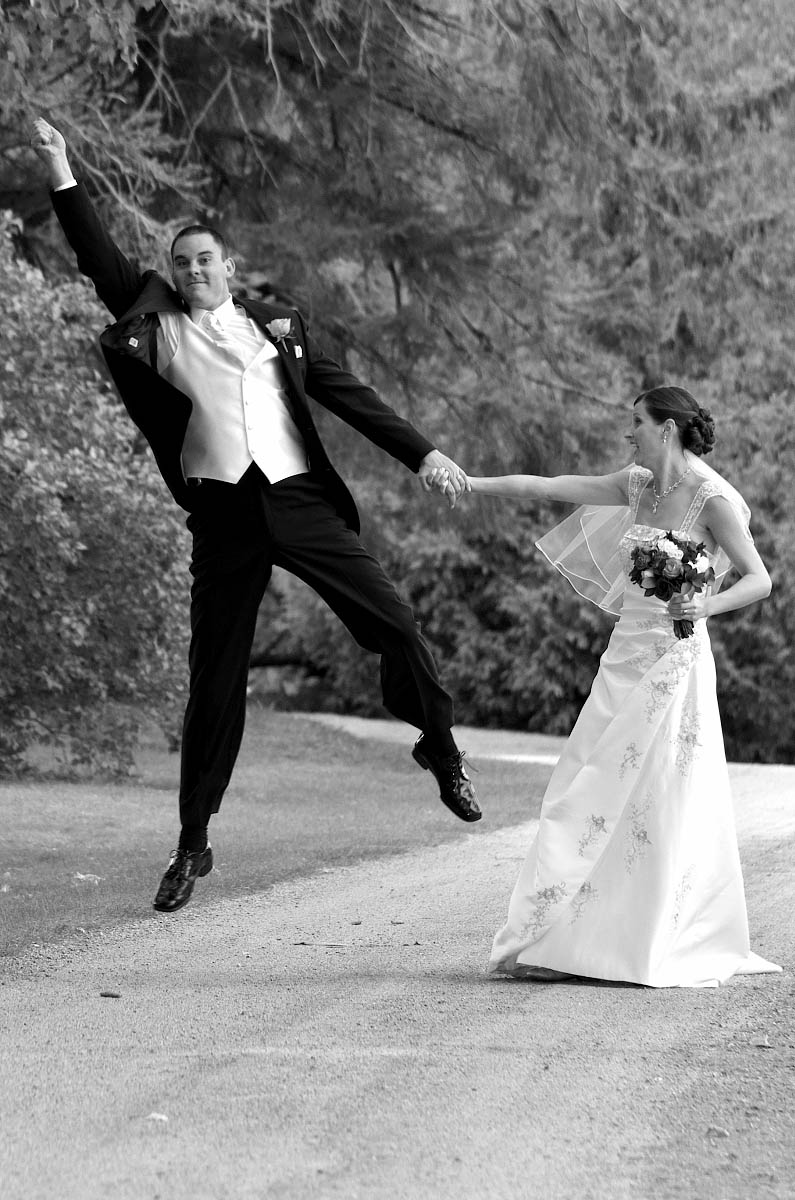 Groom leaps into the air with joy as he strolls with bride down country road at Eganridge Resort wedding in Fenelon Falls