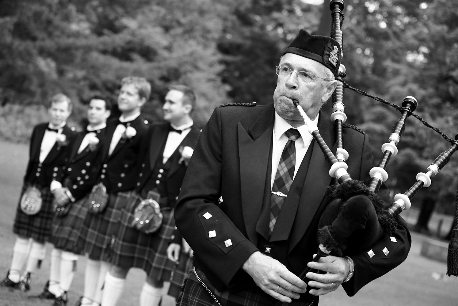 A bagpiper plays during the processional at a Kempenfelt Conference Centre wedding with Groomsman in Scottish attire wait for bride