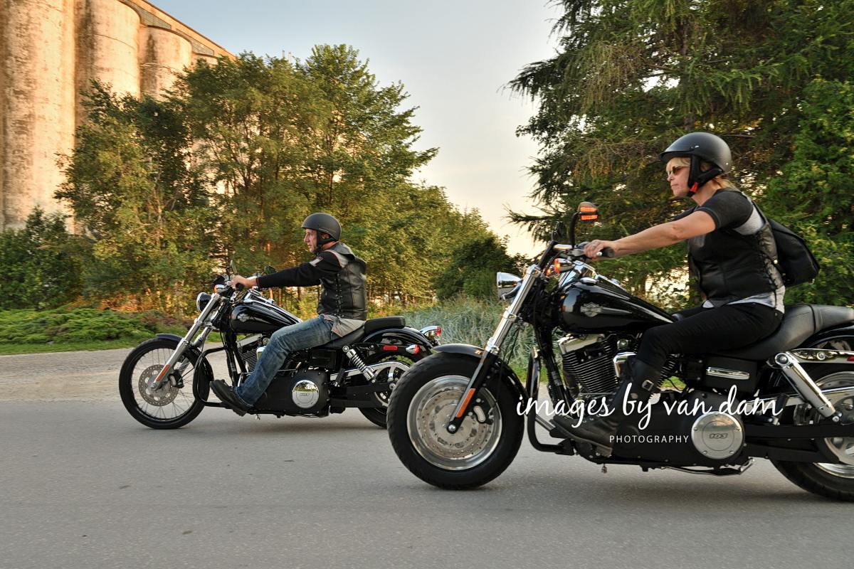 Side view of a couple riding Harley Davidson motorcycles along the road at Harbourlands Park in Collingwood