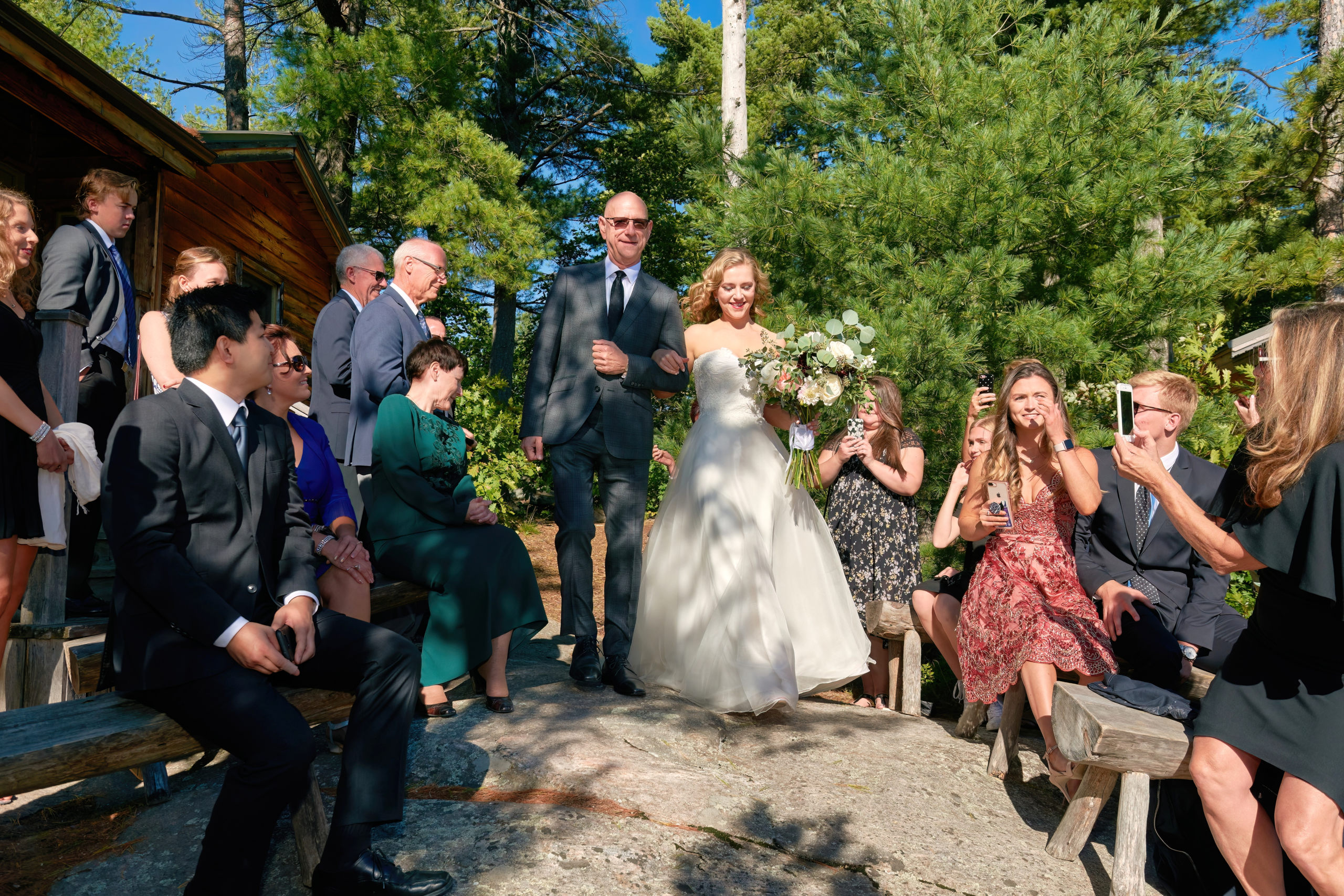 A bride walks arm in arm with her father towards the wedding alter at an outdoor wedding ceremony in French River, Ontario