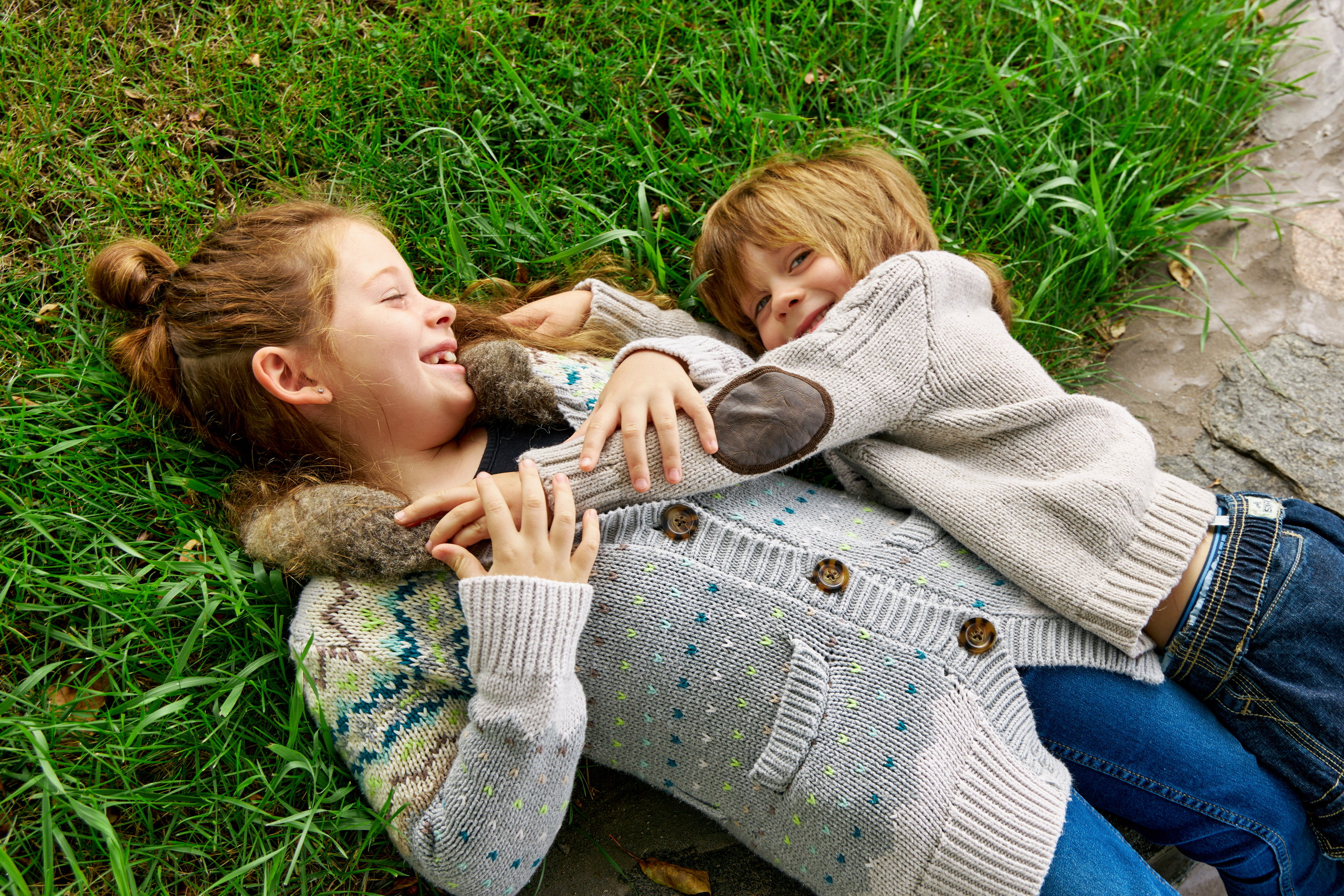 Brother and Sister Playfully Snuggle in Grass During a Family Portrait Session