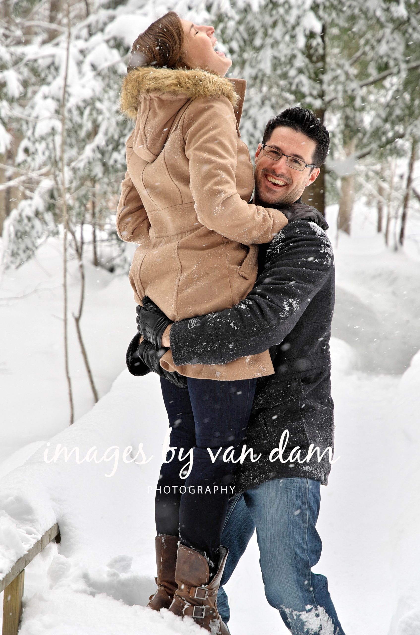 A young man sweeps up his fiancé in his arms and lifts her high into the air during a wintery engagement session near Orillia