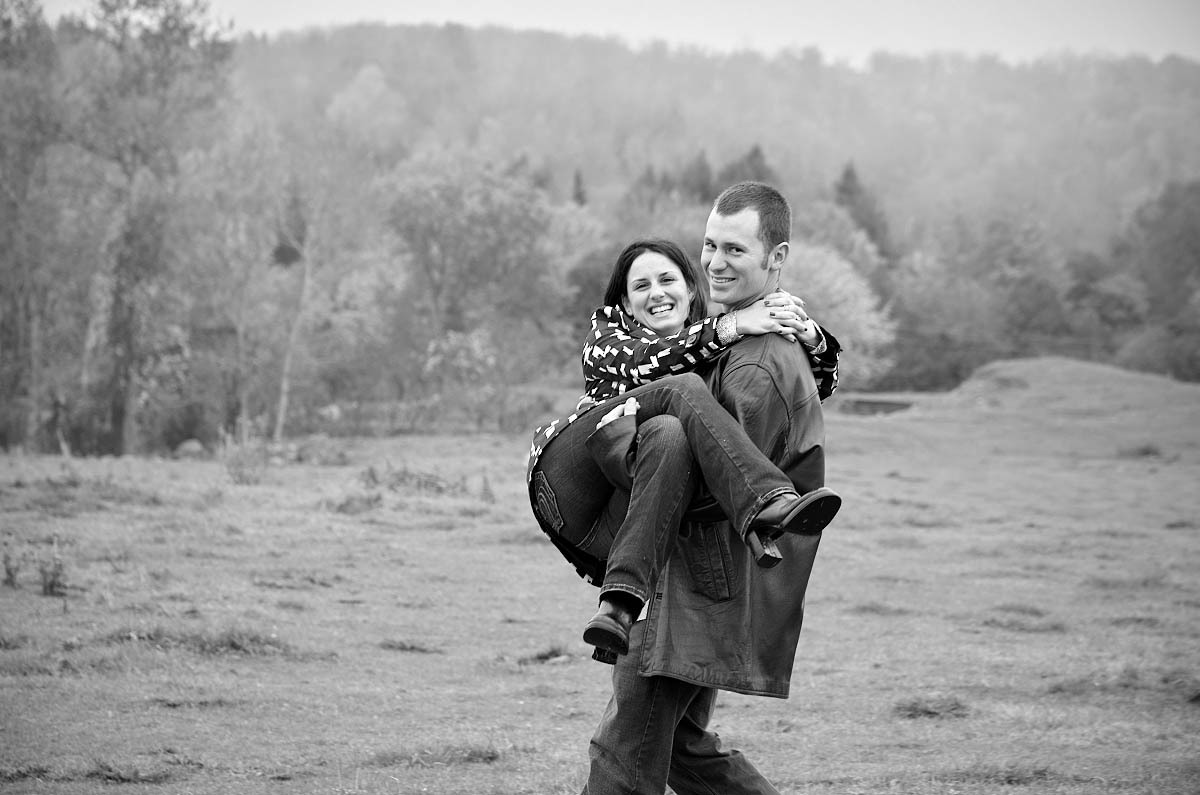 Young man carries girl in his arms through farm field
