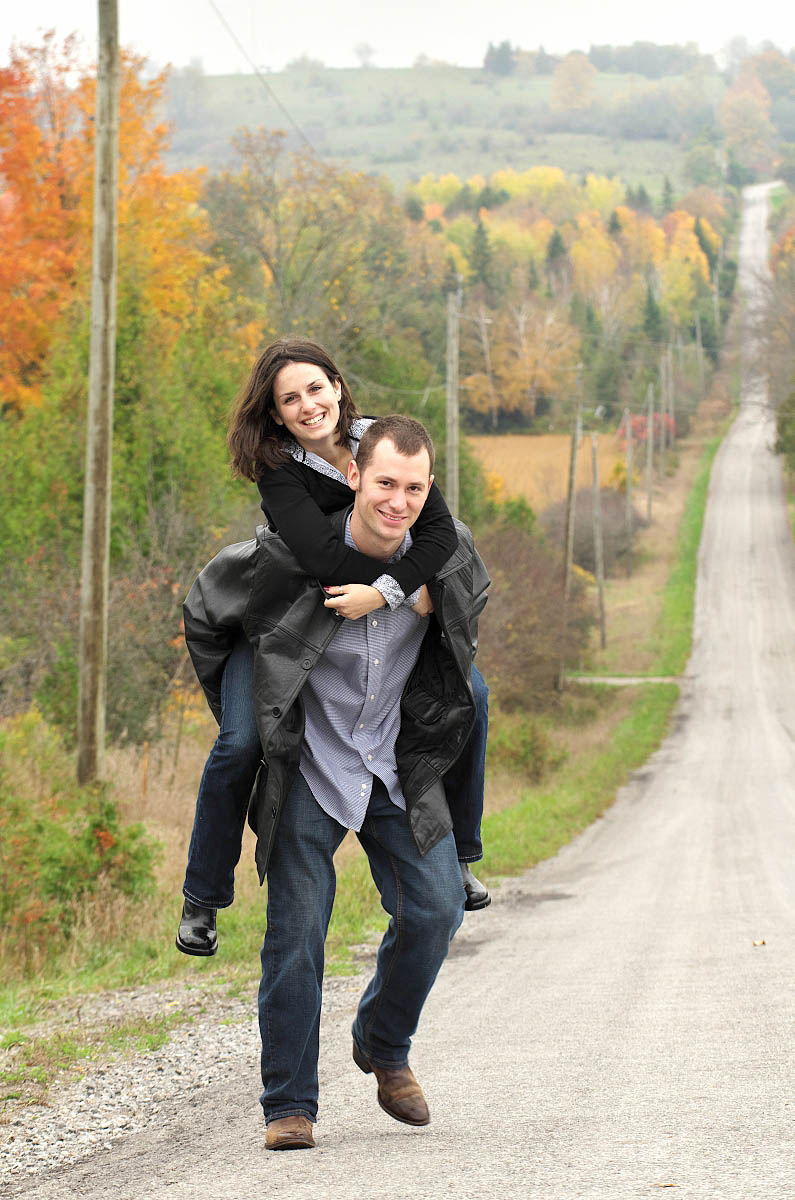 Piggybacking up a country road during Omemee country engagement session near Peterborough, Ontario