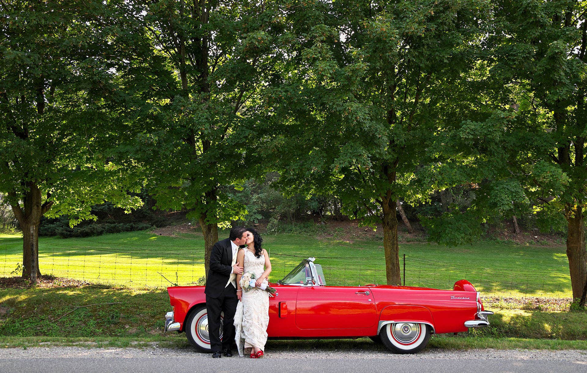 wedding couple kisses beside cherry red classic car at royal ambassador wedding in caledon ontario