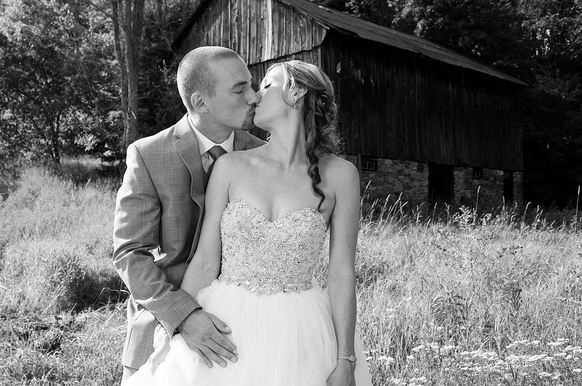 Black-and-white image of Wedding couple kissing in front of barn in Haliburton, Ontario