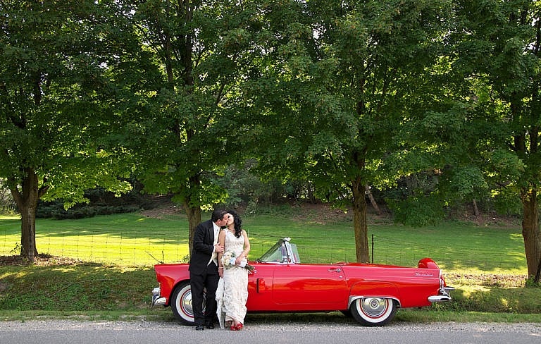 bride and groom kiss by cherry red classic car at royal ambassador wedding in caledon ontario