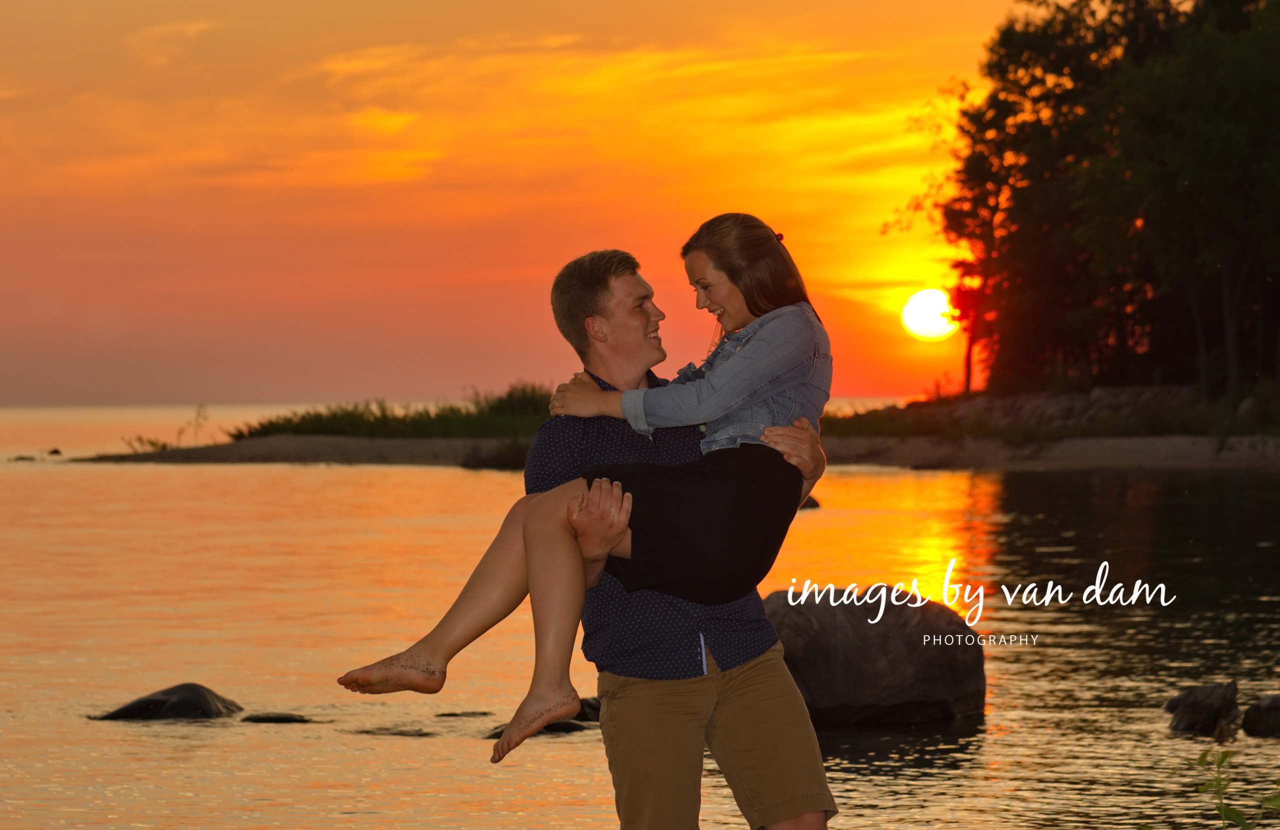 Young man lifts woman in his arm with dramatic sunset behind