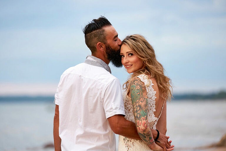 Bride looks over her shoulder while groom kisses her temple