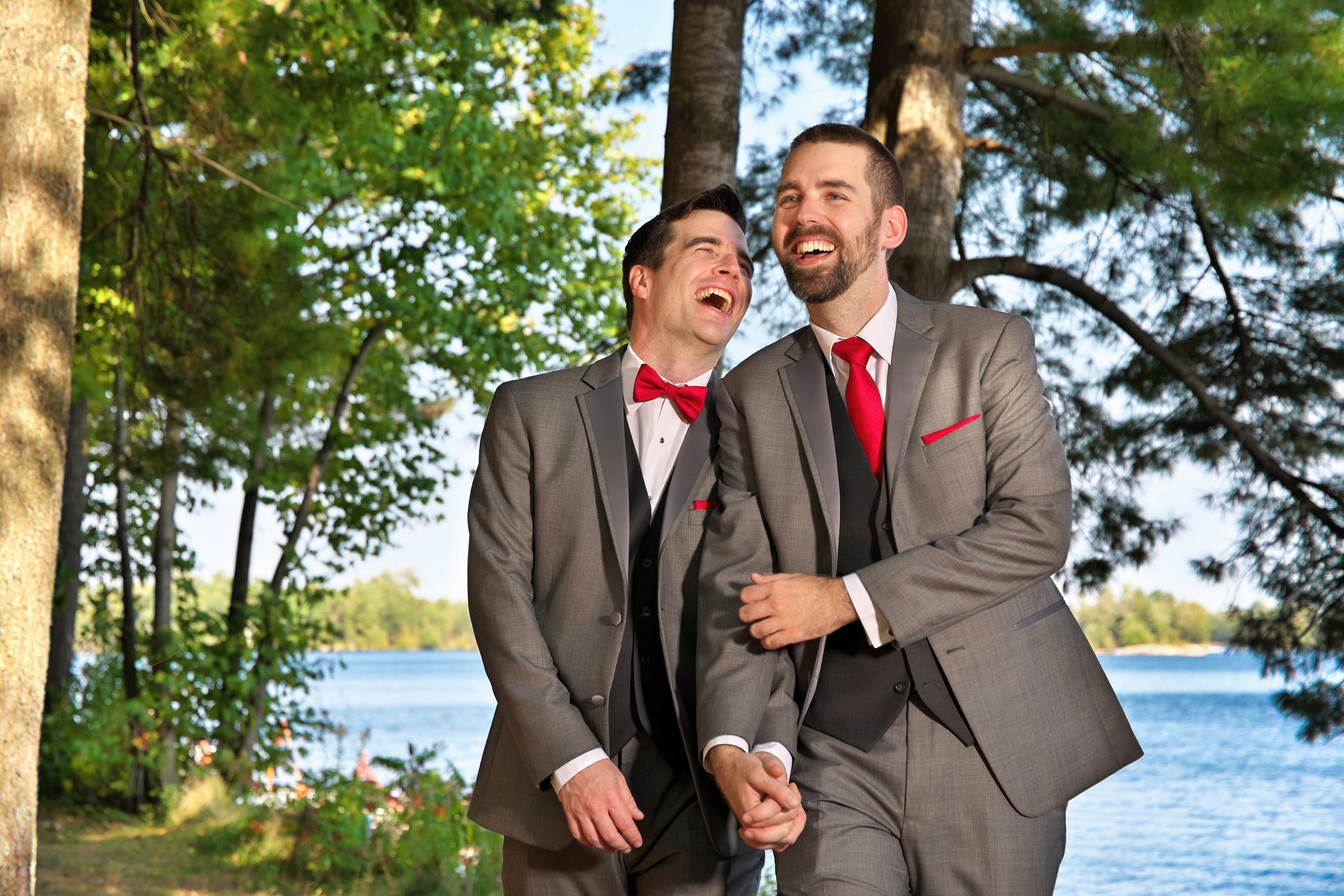 Two handsome grooms laughing and walking together along waterfront at Beachwood Resort Wedding
